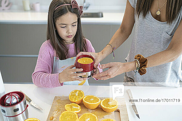 Mutter hilft Tochter bei der Zubereitung von Orangensaft in der Küche