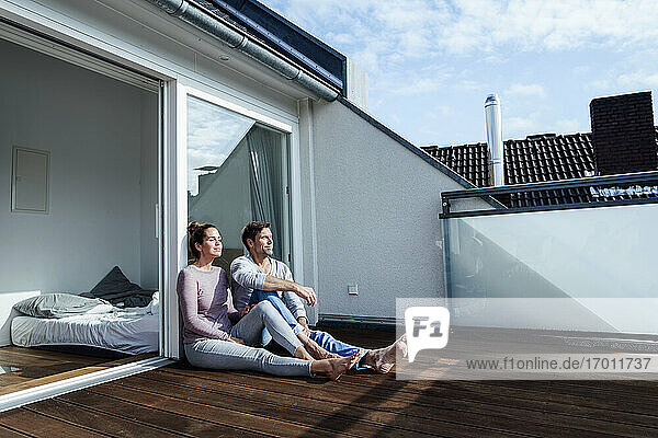 Lächelnder reifer Mann und Frau entspannen sich mit geschlossenen Augen auf dem Balkon an einem sonnigen Tag