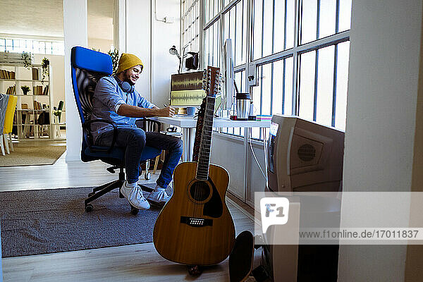 Lächelnder Songwriter  der am Schreibtisch sitzend im Studio schreibt