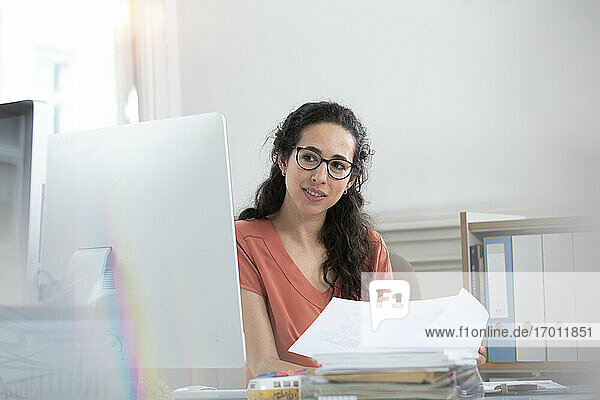 Weibliche Fachkraft  die ein Papierdokument hält und auf einen Computer im Büro schaut
