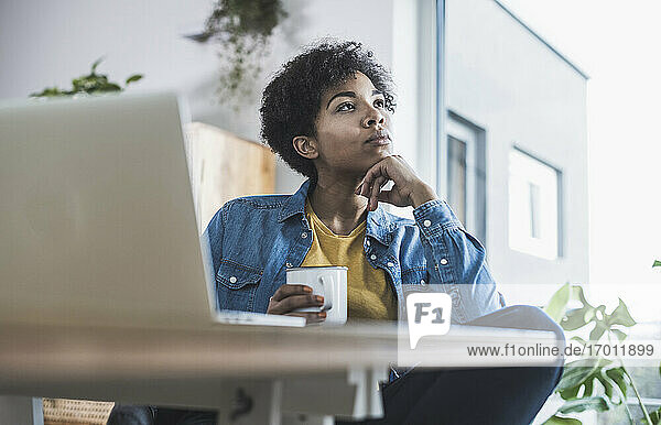 Woman holding coffee cup  sitting in front of laptop at home