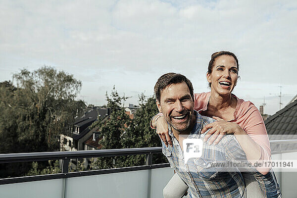 Fröhlicher reifer Mann trägt Frau huckepack auf Balkon