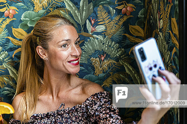 Porträt einer erwachsenen Frau  die in einem Restaurant ein Selfie mit ihrem Smartphone macht