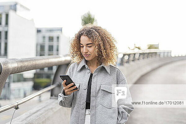 Junge Afro-Frau  die ein Smartphone benutzt  während sie auf einer Brücke in der Stadt steht