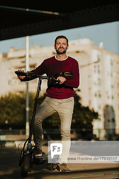 Lächelnder Mann mit Elektro-Scooter in der Stadt stehend