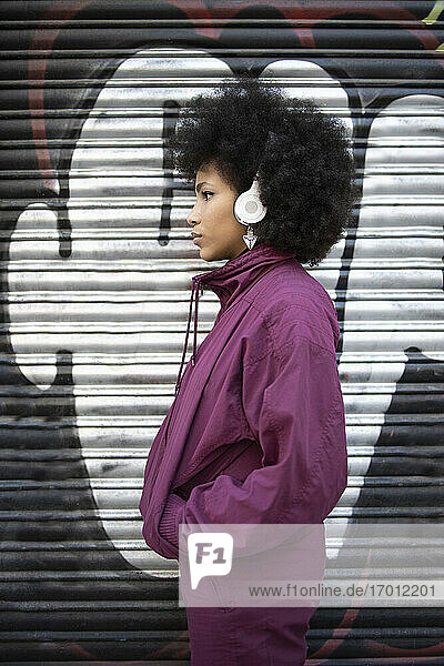 Afro-Frau mit Händen in den Taschen  die Musik hört  während sie an einer Graffiti-Wellwand steht