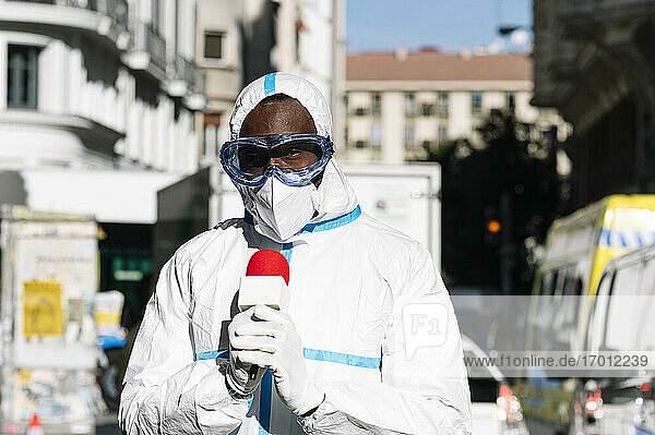 Male presenter wearing protective suit with microphone standing in city