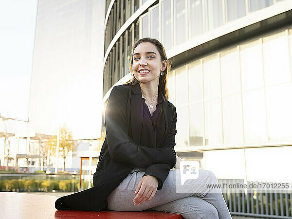 Young businesswoman smiling while sitting on bench in city