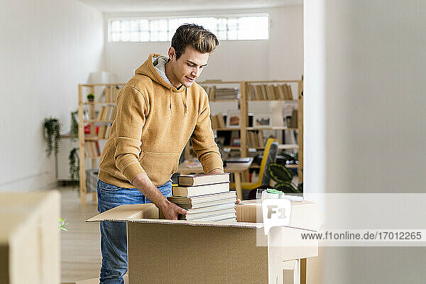 Junger Mann packt Bücher in Pappkarton in neuer Dachgeschosswohnung
