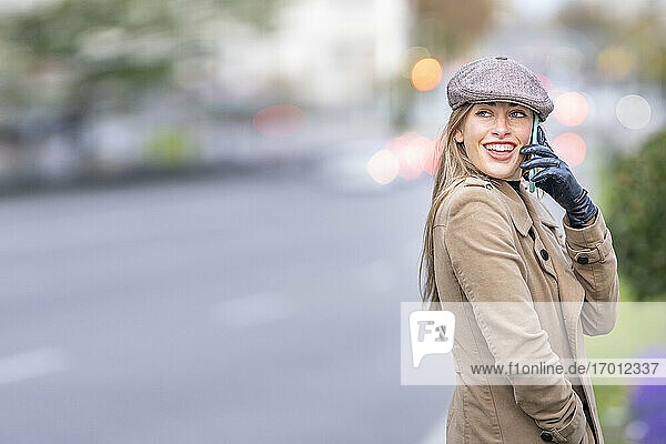 Lächelnde attraktive Frau  die auf der Straße steht und mit einem Smartphone spricht