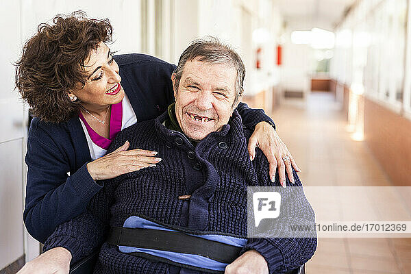 Happy nurse looking at disabled man in corridor of nursing home