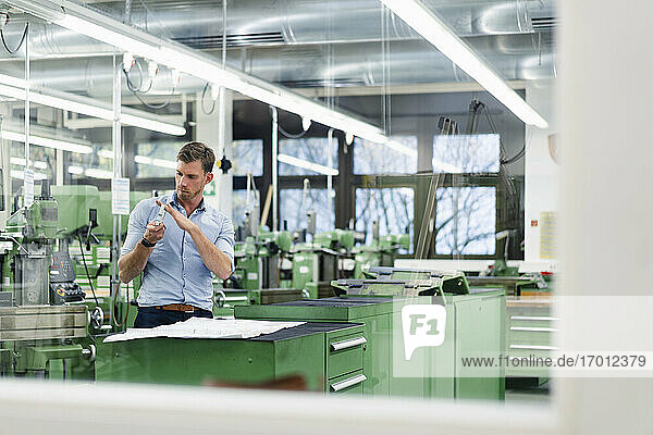 Männlicher Fachmann mit Blaupause Überprüfung Maschine Teil durch Glas in der Fabrik gesehen