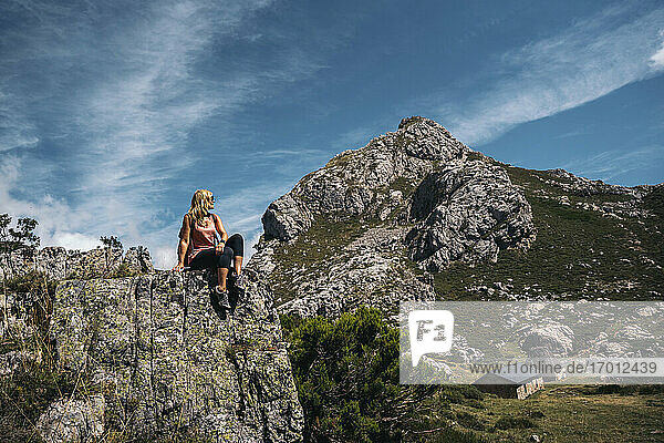 Frau schaut weg  während sie an einem sonnigen Tag auf einem Felsenberg sitzt