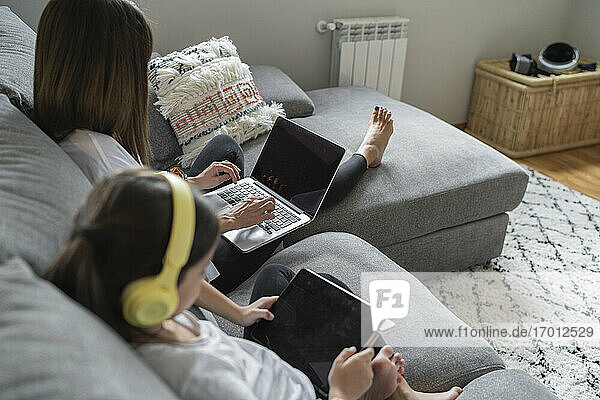 Tochter mit digitalem Tablet  während die Mutter zu Hause einen Laptop benutzt