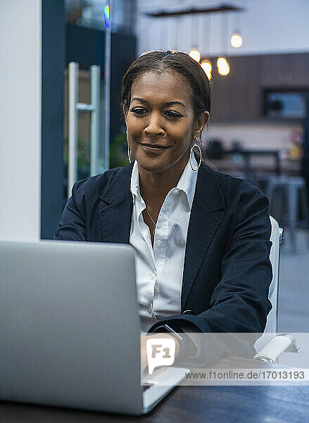 Lächelnde Geschäftsfrau arbeitet am Laptop am Schreibtisch im Büro