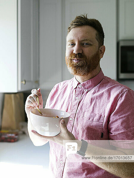 Porträt eines Mannes  der in der Küche Müsli frühstückt