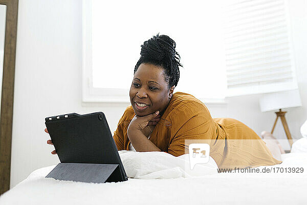 Lächelnde Frau auf dem Bett liegend und mit Tablet