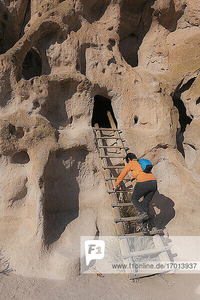 USA  New Mexico  Bandelier National Monument  Frau klettert Leiter zu Felsenwohnungen in Bandelier National Monument