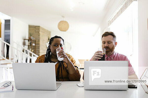 Mann und Frau trinken Wasser bei der Arbeit mit Laptops im Home-Office