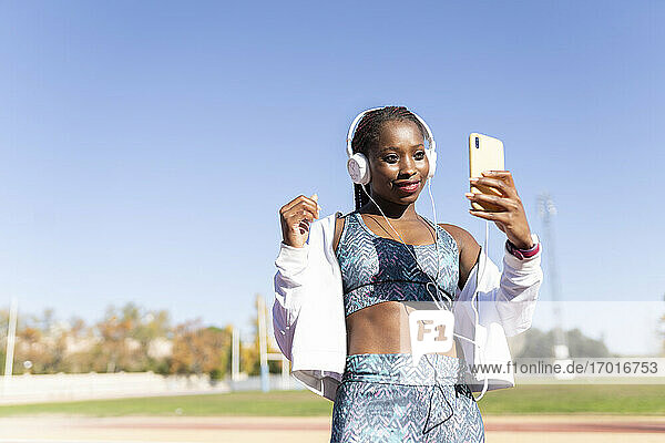 Sportlerin hört Musik  während sie ein Selfie mit ihrem Smartphone gegen den klaren Himmel macht