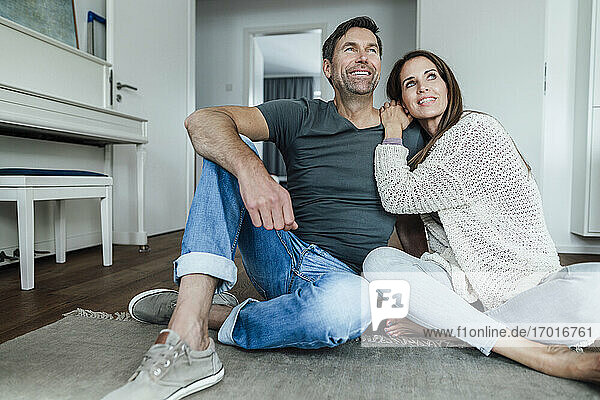 Smiling mature couple day dreaming while sitting on floor at home