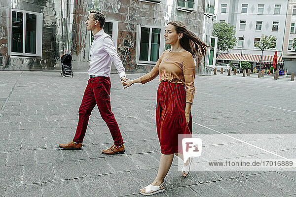 Heterosexuelles Paar hält sich an den Händen  während es auf der Straße in der Stadt spazieren geht