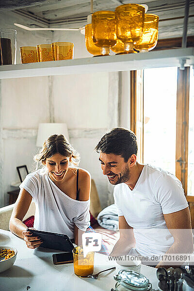 Glückliches junges Paar  das beim Frühstück zu Hause ein Tablet betrachtet