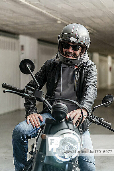 Gut gelaunter Mann mit Helm und Sonnenbrille auf einem Motorrad auf einem Parkplatz sitzend
