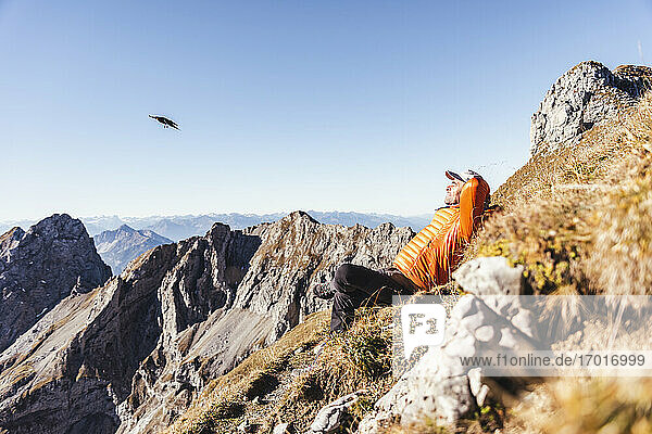 Male hiker relaxing on mountain against clear sky during sunny day