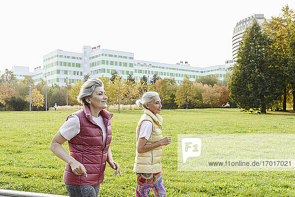 Lächelnde Freundinnen laufen im öffentlichen Park an einem sonnigen Tag