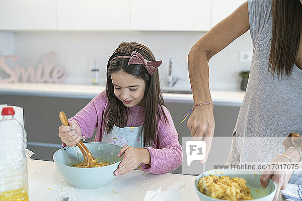 Tochter bereitet Muffin zu und steht neben ihrer Mutter in der Küche