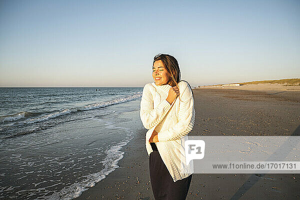 Happy young woman at beach against clear sky during sunset