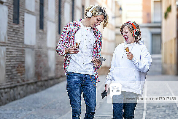 Lächelnde Freunde mit Eiscreme  die ein Handy benutzen  während sie auf dem Fußweg gehen