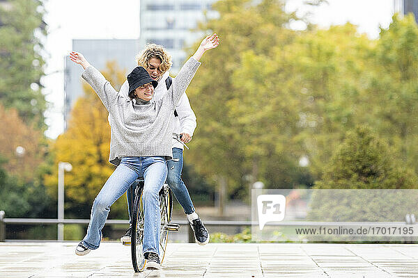 Unbeschwerte Frau sitzt mit einem männlichen Freund auf einem Fahrrad im Park