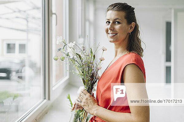 Porträt einer lächelnden Frau mit Blumen am Fenster