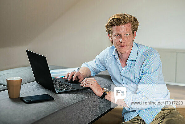 Male entrepreneur with laptop by couch in living room