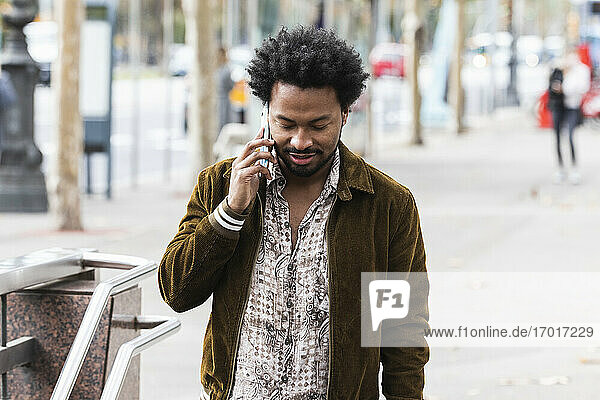Man with afro hair communicating over smart phone while standing on footpath