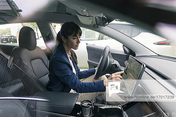 Ältere Geschäftsfrau  die in einem Elektroauto sitzend durch ein Gerät navigiert