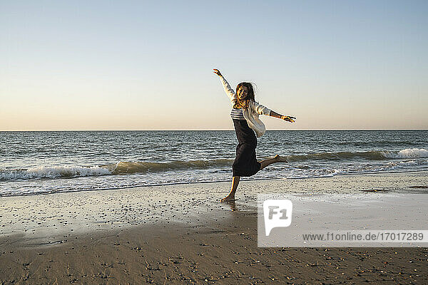 Sorglose Frau läuft am Strand gegen den klaren Himmel bei Sonnenuntergang