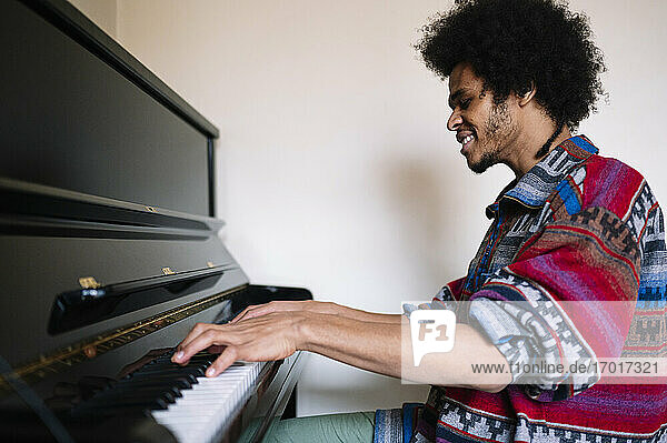 Lächelnder männlicher Musiker beim Üben am Klavier im Wohnzimmer