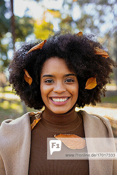 Curly hair woman with dry leaf on hair smiling while standing at park