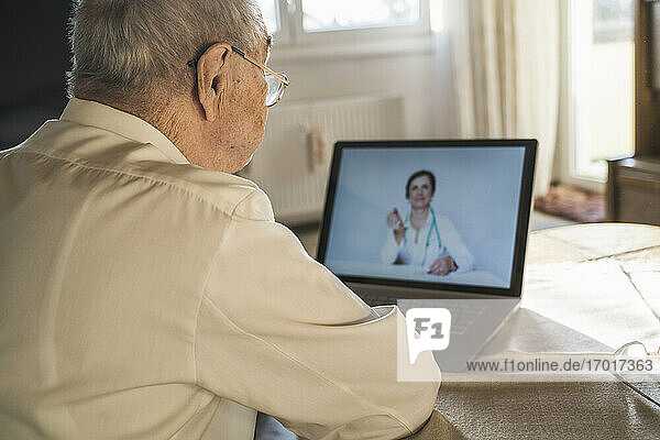 Älterer Mann lässt sich von einer Ärztin auf Video über einen Laptop im Wohnzimmer beraten