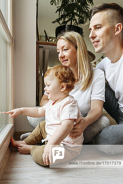 Glückliche Familie mit kleiner Tochter schaut durch das Fenster
