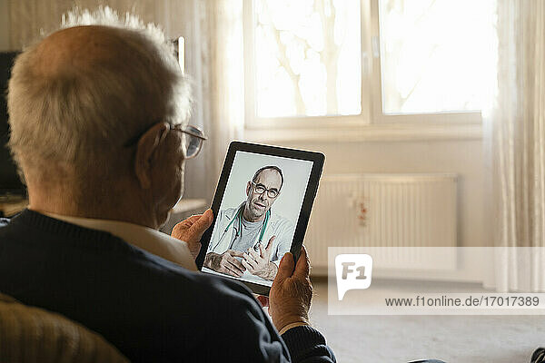 Allgemeinmediziner berät älteren Mann online über ein digitales Tablet im Wohnzimmer