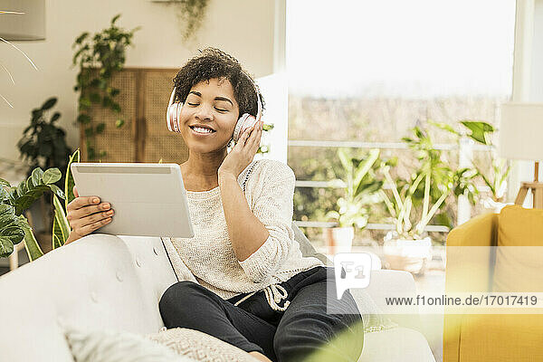 Junge Frau mit Kopfhörern  die Musik hört  während sie ein digitales Tablet benutzt  das zu Hause steht