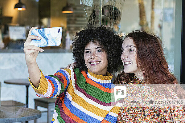 Lächelnde Freunde  die ein Selfie mit ihrem Mobiltelefon machen  während sie im Restaurant sitzen