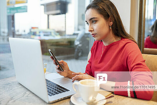 Frau mit Smartphone und Laptop in einem Café