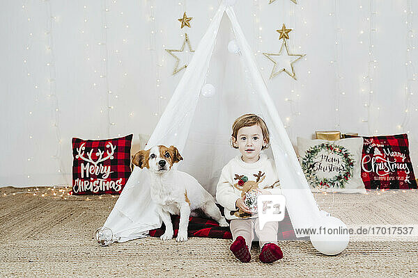 Cute Baby-Mädchen mit Welpen sitzen im Zelt gegen Weihnachtsschmuck zu Hause