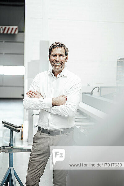 Confident businessman with arms crossed standing in workshop at industry