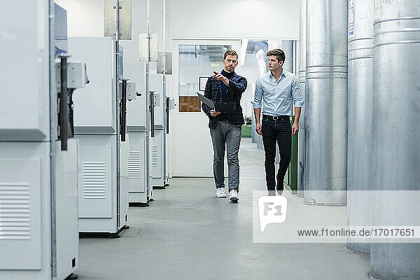 Männliche Mitarbeiter diskutieren über Maschinenausrüstung  während sie in der Fabrik spazieren gehen